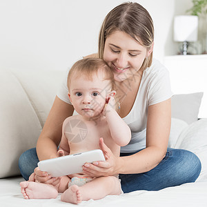 使用平板电脑尿布涂的母亲和可爱婴儿男孩高清图片