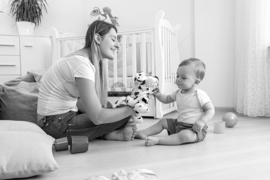 美丽的年轻母亲和10个月大的婴儿子与地板上的木偶玩耍黑色和白画面图片