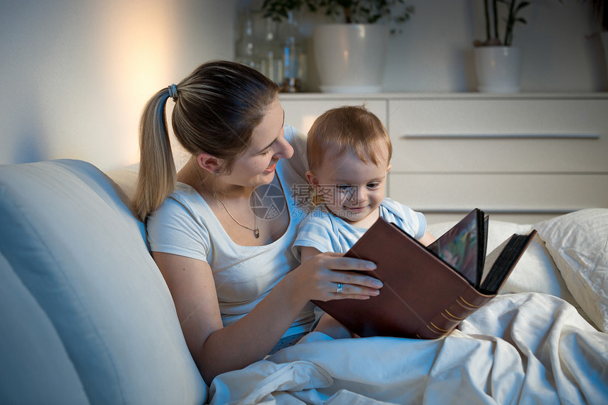 美丽的母亲在睡觉前微笑着读故事给儿子看图片