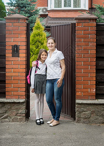 微笑的母亲抱着女儿在家门口上学家庭高清图片素材