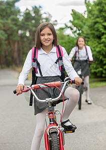 两个穿着校服的快乐女孩早上骑自行车图片