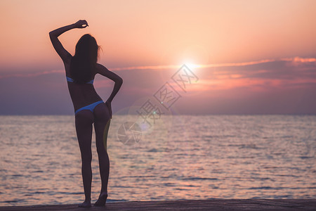 美丽的女人在海洋日出背景的周光下图片