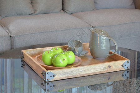 绿色苹果和陶瓷杯放在灰色沙发旁边玻璃顶桌的木灰色沙发上图片
