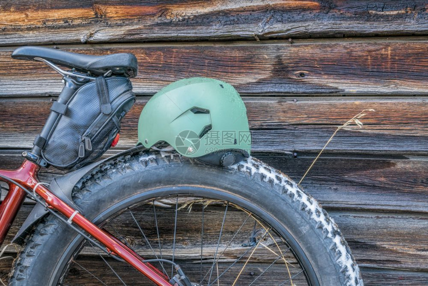 长脚自行车轮马鞍和头盔与生锈的木小墙相对图片