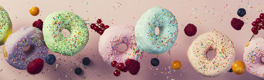 甜圈喷洒和浆果在粉色糊面背景下落或飞起来图片