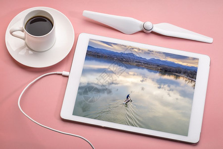 在湖边的浮板上起立在湖边的空中景象上在湖边的浮板上在黄昏时科罗拉多州落基山脚下一个平静的湖泊上划桨用咖啡来审查数字平板上的空中图背景图片