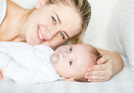 快乐微笑的妈和婴儿躺在床上看着镜头图片