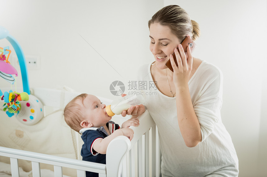 微笑的年轻女商人通过电话说和喂养其小儿子的肖像微笑年轻女商人通过电话说和喂养其小婴儿的肖像图片