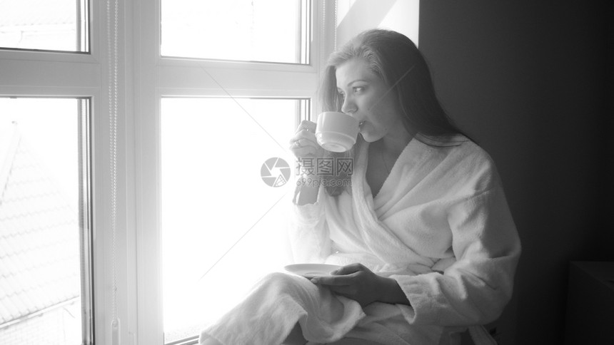 坐在窗户和喝茶的年轻妇女黑白画像坐在窗户和喝茶的年轻妇女单色画像图片