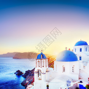 希腊圣托里尼岛奥亚镇日落时传统和著名的白色房子和教堂在爱琴海的卡尔德拉岛上空有蓝色圆丘陵背景