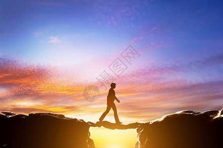 一个人在两座山之间的悬崖上行走另一个人充当桥梁日落商业概念图片