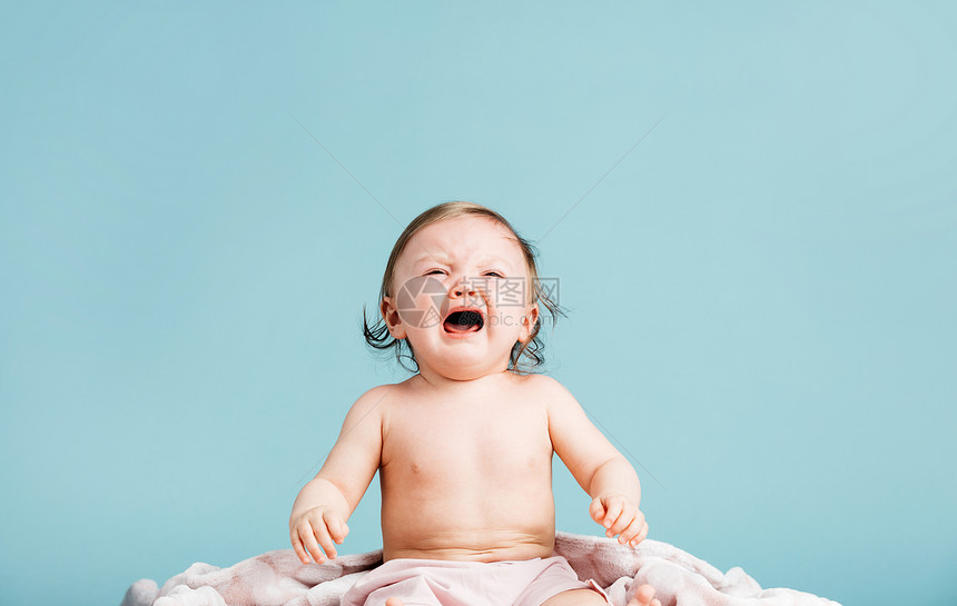 坐在蓝色背景的毯子上哭泣女婴童年概念坐在毯子上哭泣的女婴图片