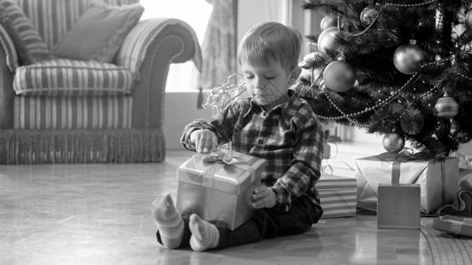 坐在圣诞树下礼物盒上拉弓的可爱幼儿男孩黑白照片背景图片