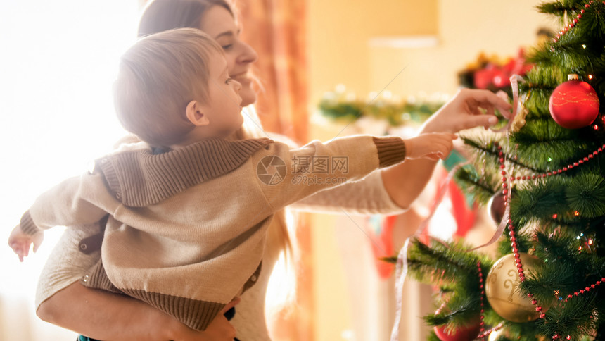 微笑的年轻母亲与小儿子一起装饰圣诞树的肖像快乐微笑年轻母亲与小儿子一起装饰圣诞树的肖像图片