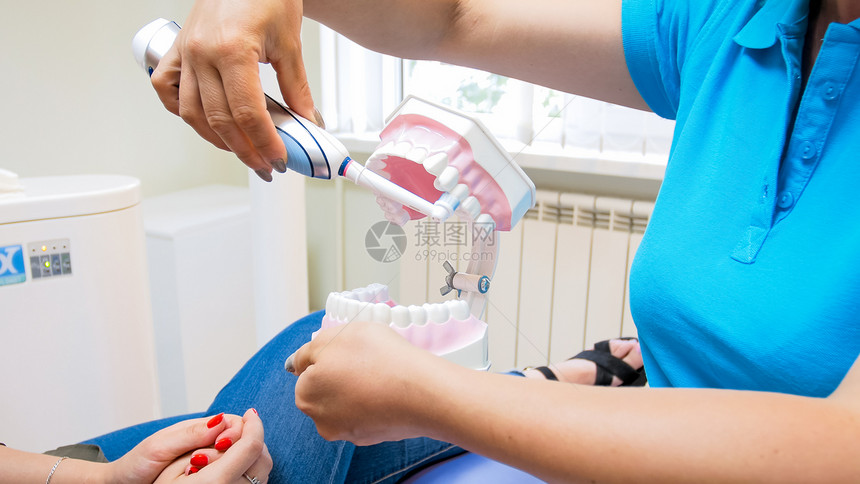 牙科医生用电刷对病人进行洗牙教育的近视图像牙科医生用电刷对病人进行洗牙教育的近视照片图片
