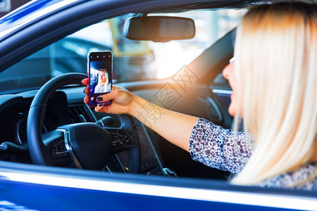 年轻快乐笑的女司机在现代豪华轿车的智能手机上拍摄自照片微笑高清图片素材