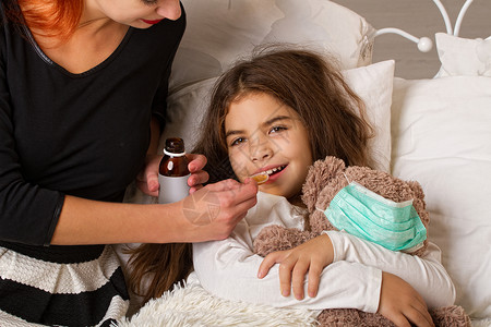微笑的小女孩与最喜欢的泰迪熊他们穿上一个纱布绷带躺在床上生病她妈正在喝的药背景图片