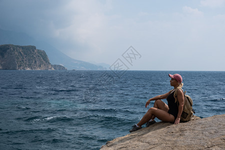 一个金发女孩坐在山顶看着海滩放松自然旅行岩石高清图片素材