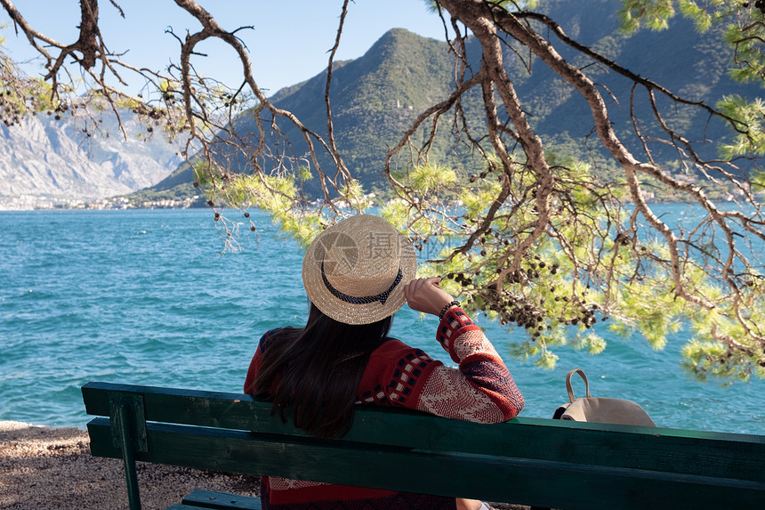 穿着帽子的女孩坐在靠近水的木制码头上暑假旅行概念图片