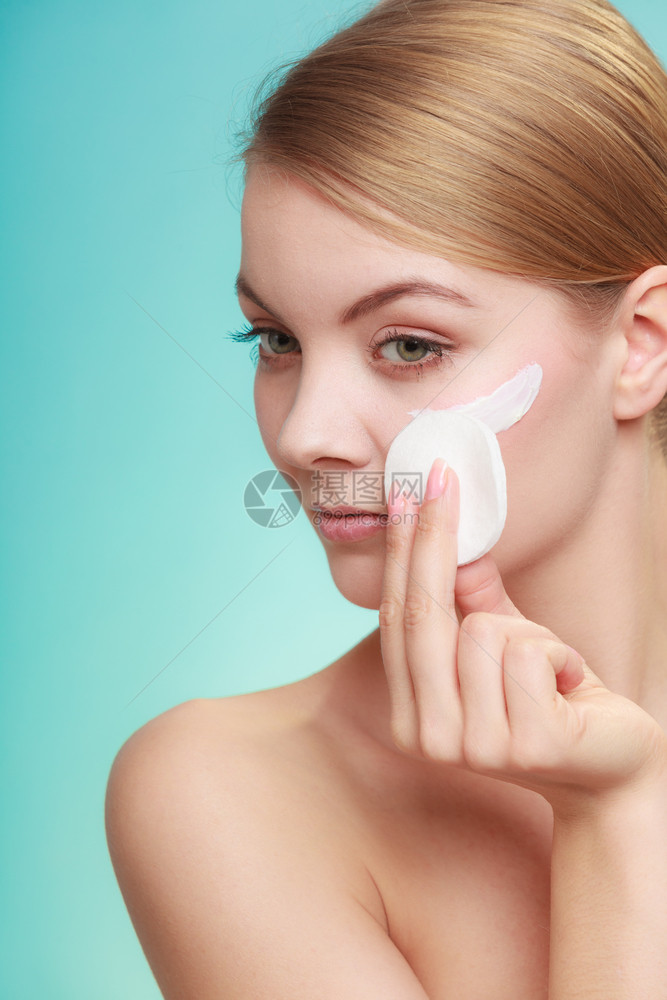 妇女用棉布垫子从脸上抹去化妆品年轻女孩照顾皮肤护理概念工作室拍摄在蓝色上妇女用奶油和棉垫擦除化妆品图片