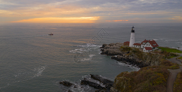 一艘渔船在日出时伊丽莎白角波特兰正灯附近沿着海岸航行美国高清图片素材