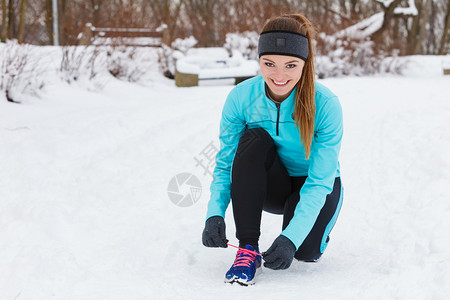 年轻女孩在雪地里蹲下系鞋带准备跑步图片