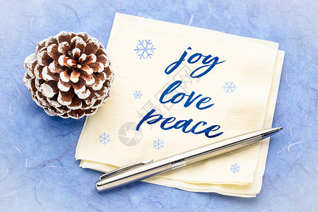圣诞蓝色欢乐爱和平概念纸巾上的笔迹用松锥形装饰和蓝色木莓纸背景