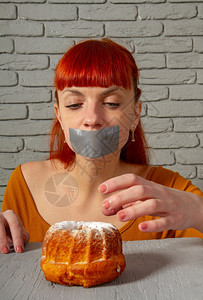 一位年轻红头发女孩的概念形象坐在饮食中与她的嘴边面对高清图片素材