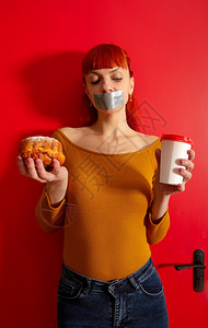 一位年轻红头发女孩的概念形象坐在饮食中与她的嘴边室内的高清图片素材