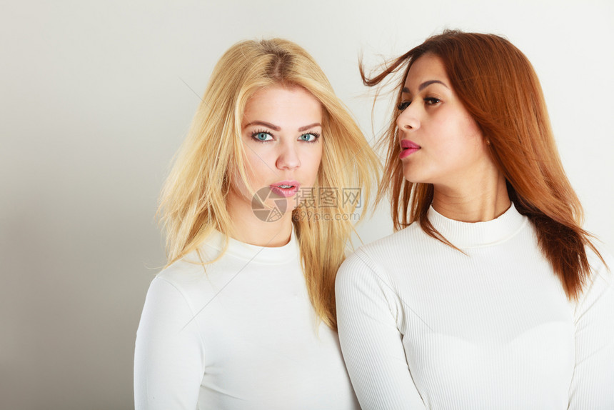 朋友的概念两个年轻朋友在一起女孩有白色的顶部站在对方旁边一个女人有金发第二个黑两年轻朋友在一起图片