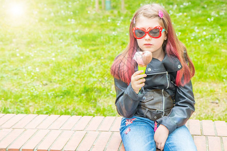 带着墨镜的笑小女孩在公园吃冰淇淋凉爽的高清图片素材