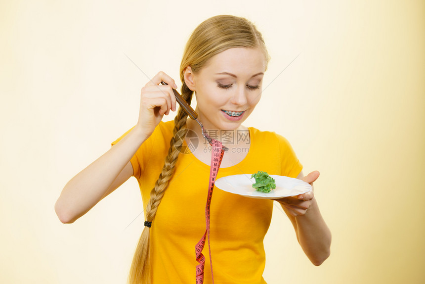 快乐的年轻微笑女士即将用胶带制成的盘子和叉来吃生菜图片