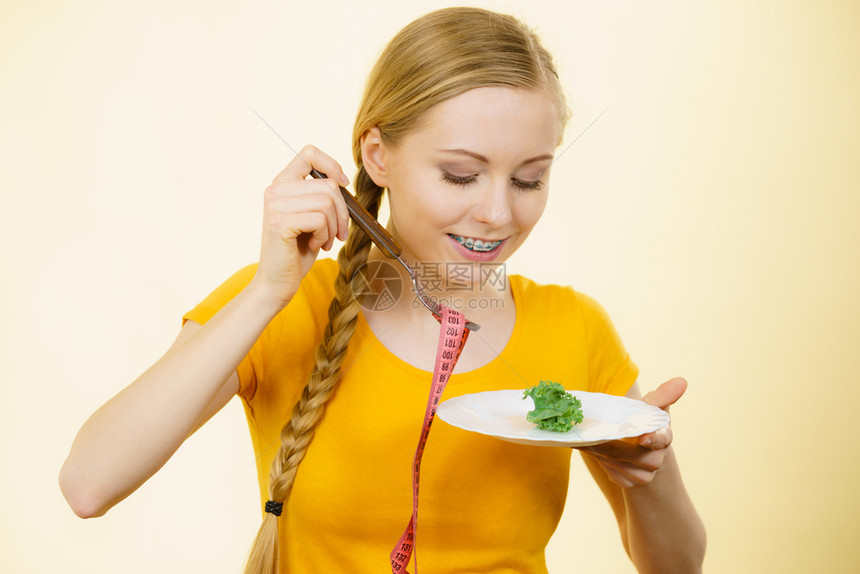 快乐的年轻微笑女士即将用胶带制成的盘子和叉来吃生菜图片