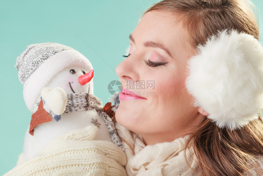 带着小雪人微笑可爱的女人戴着耳巾和围的迷人女孩在绿色工作室冬天时装带着小雪人微笑可爱的女人冬天图片