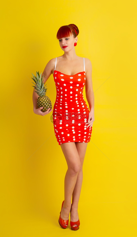 穿着波卡点装的红头发漂亮女孩手里拿着菠萝黄褐色的背景图片