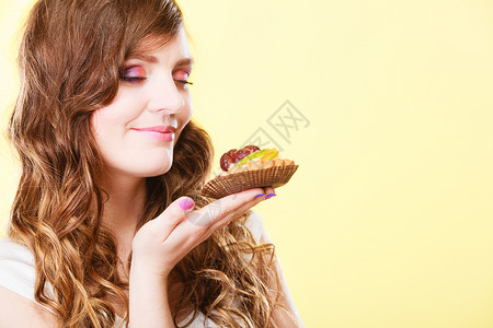 可爱的闭着眼睛女人手握着蛋糕闻黄色背景的味道图片