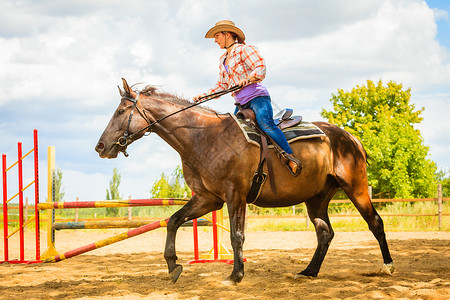 牛仔帽女在阳光明媚的白天骑马穿越障碍图片