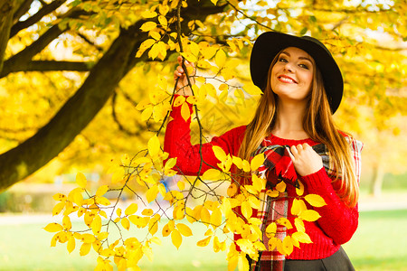 美丽的年轻女子在秋天公园行走时装女孩穿着红色毛衣围巾和黑帽子穿着红色围巾和黑帽子在秋天公园行走的迷人女子在秋天公园行走背景图片