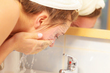 在浴室用清洁水洗脸的妇女照顾外衣的孩早间卫生皮肤护理治疗在浴室洗脸的妇女卫生背景图片