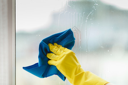 女用黄色手套蓝抹布和喷雾洗涤剂用黄色手套打扫窗户春季清洁家务工作概念使用洗涤剂擦家庭窗户背景图片