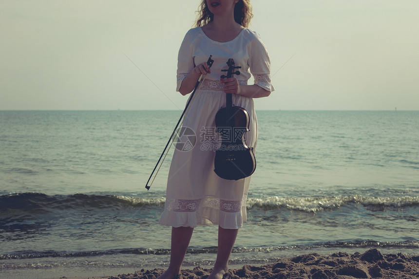音乐爱好和日常激情概念海边滩上的妇女拿着小提琴海边滩上的妇女拿着小提琴海边的妇女拿着小提琴图片