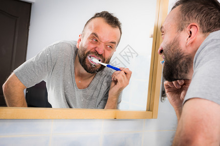 成人男子在清晨卫生例行活动期间在洗手照着浴室镜子刷牙男在洗手间刷牙图片