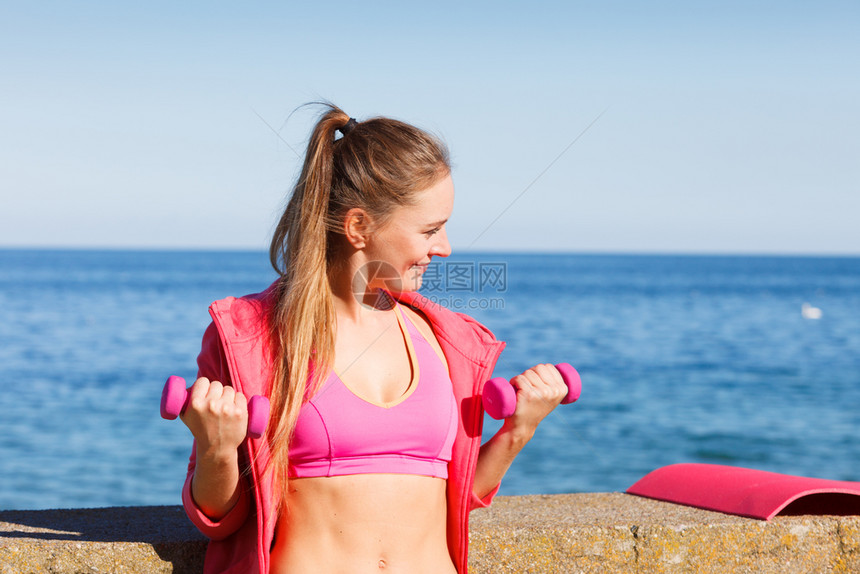 女在户外与哑铃一起运动女在海边运动中穿服的健身女孩在户外与哑铃一起运动图片