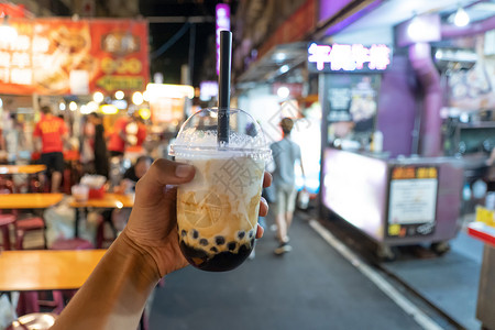 手冰手握着冰奶茶塑料杯底泡沫模糊在夜市的传统饮料背景