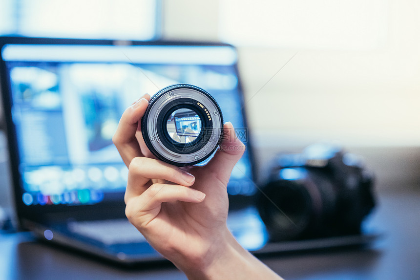 摄影师手上拿着专业的光学照片镜头和笔记本电脑在模糊的背景中图片