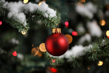 传统人造圣诞树带有红球装饰品有彩色明灯和背景雪图片
