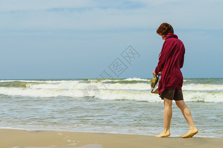 在温暖的秋天气下妇女有闲暇时间在海滩上赤脚徒步行手握鞋凉图片