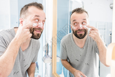 男人在浴室镜子前脸上涂满了香水男人在浴室里涂了润湿霜背景图片