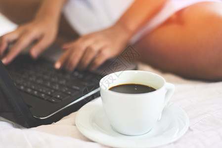 早上在床用笔记本电脑与妇女一起用笔记本电脑在床上喝咖啡杯图片