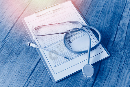 胸腔镜和在医疗记录上的笔医院木制桌子上的体检报告健康查概念背景图片